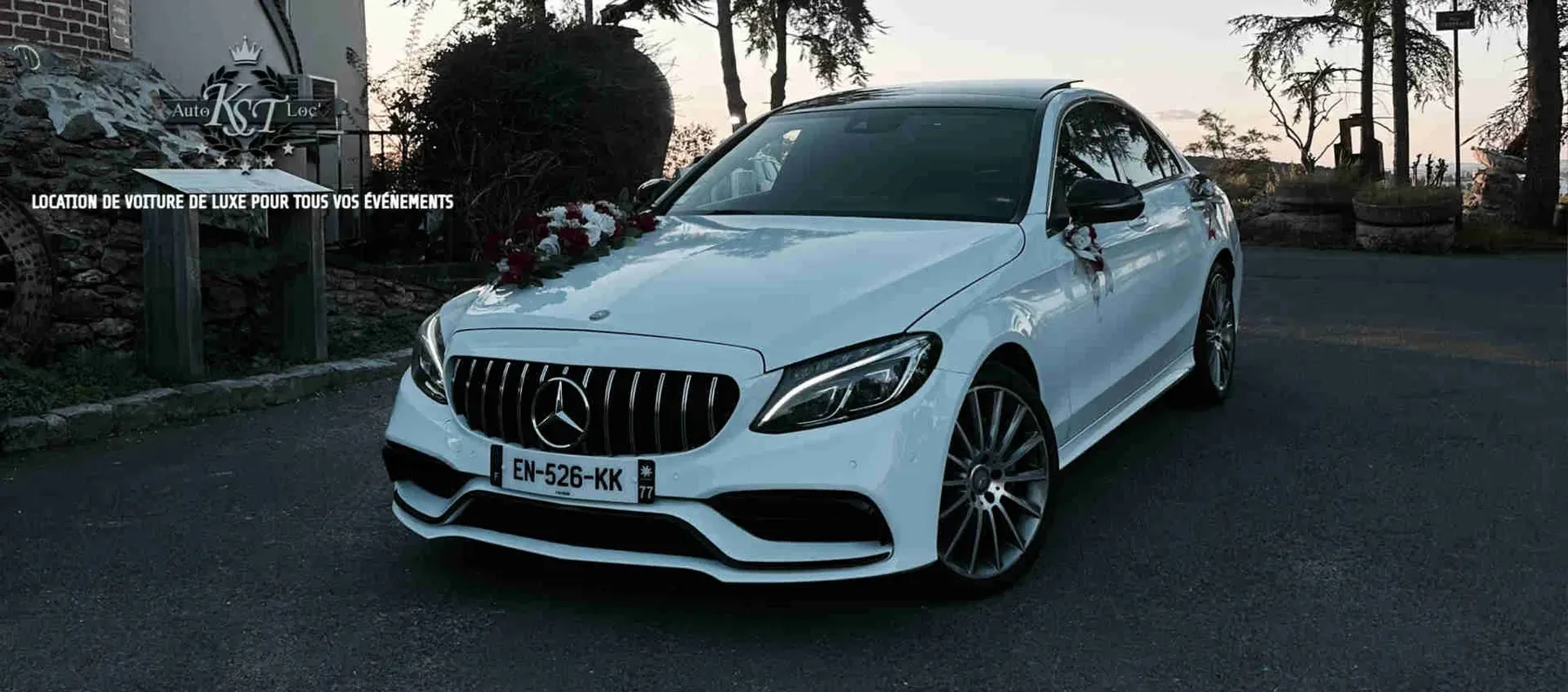 Mercedes Classe C blanche décorée d'un bouquet de fleurs rouges et blanches, vue avant au crépuscule
